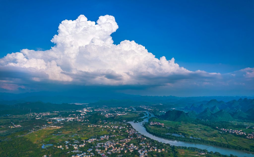 Stunning aerial view of Guilin's landscape featuring lush greenery, river, and dramatic clouds.
