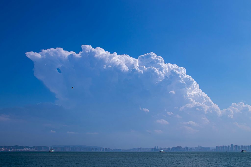 Majestic cumulus clouds towering over a calm sea and city skyline, showcasing a serene blue sky.