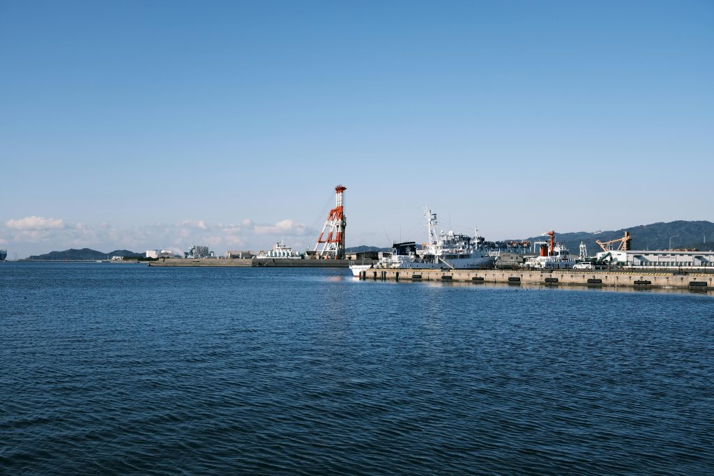 A peaceful view of Gamagōri harbor featuring ships docked at the pier under clear blue skies.