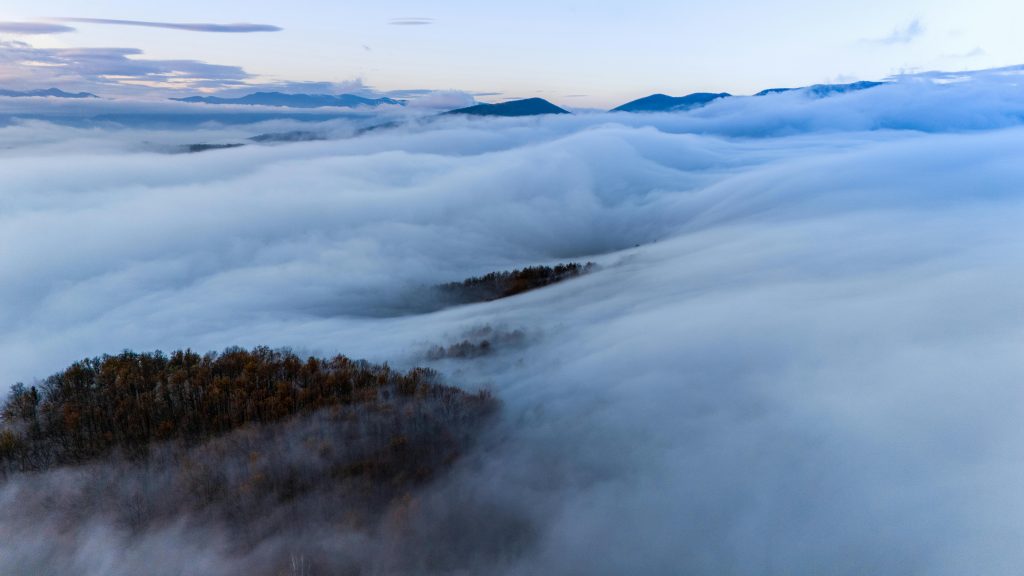 Aerial view of mountains blanketed in serene mist during sunrise, creating a dreamlike atmosphere.
